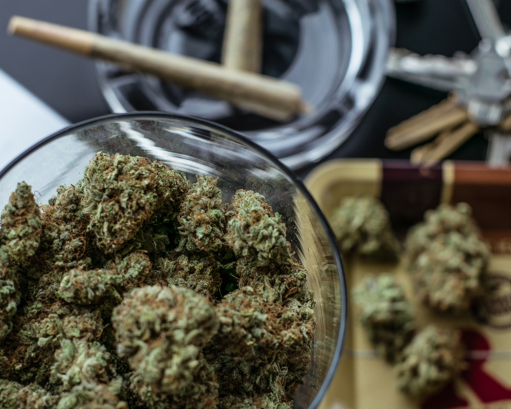 Jars of cannabis buds with some joints in the background