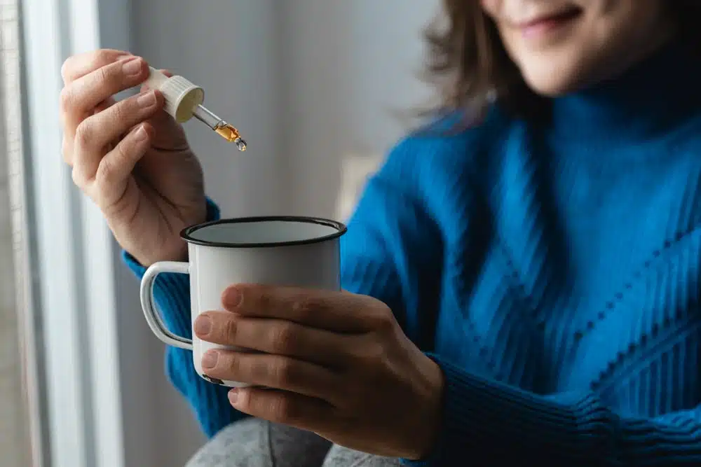 Woman adding cannabis tincture to her drink with a dropper