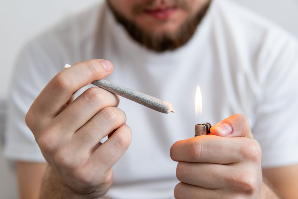 A bearded man holding a hash joint with a lit lighter.