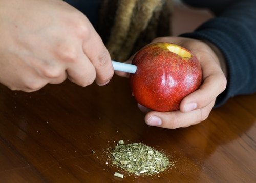 A man with dreadlocks making and apple bong on a wooden desk