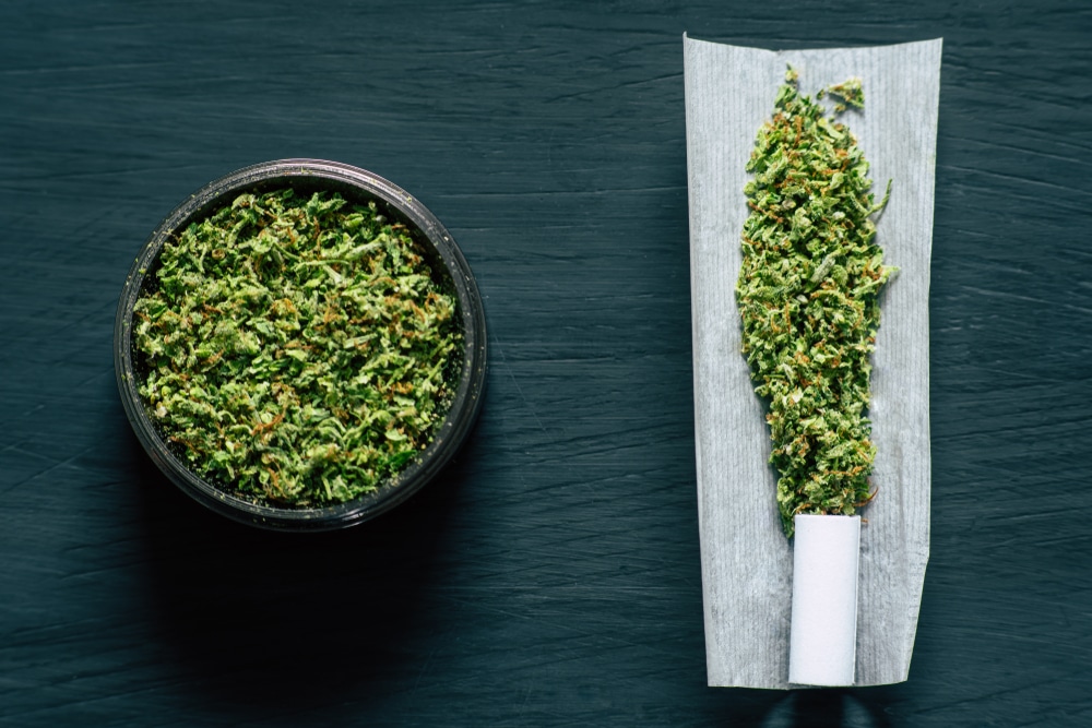 ground cannabis bud in a grinder next to a ready-to-roll joint