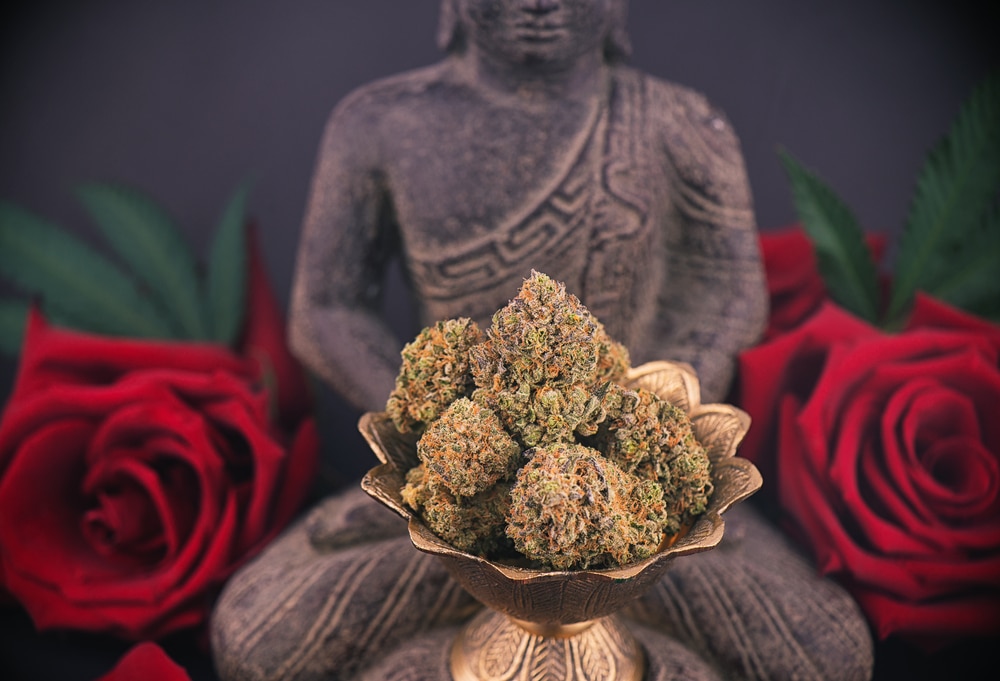 statue of man meditating behind a bronze bowl of weed buds