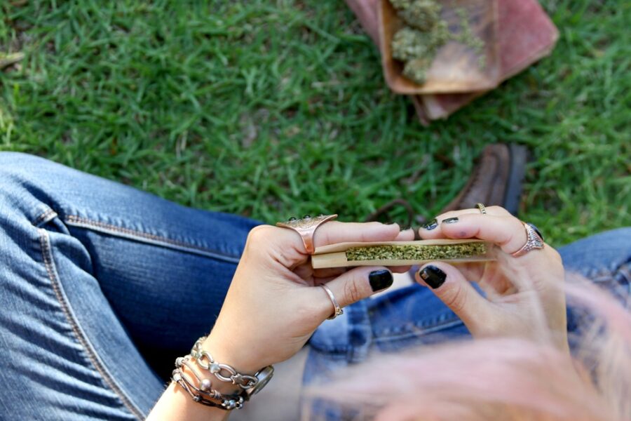 a woman rolling a joint outside on a lawn